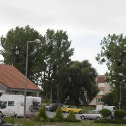 Zewnętrzny ekran LED z wyświetlaną reklamą na ścianie budynku, widok z ulicy z zaparkowanymi samochodami.