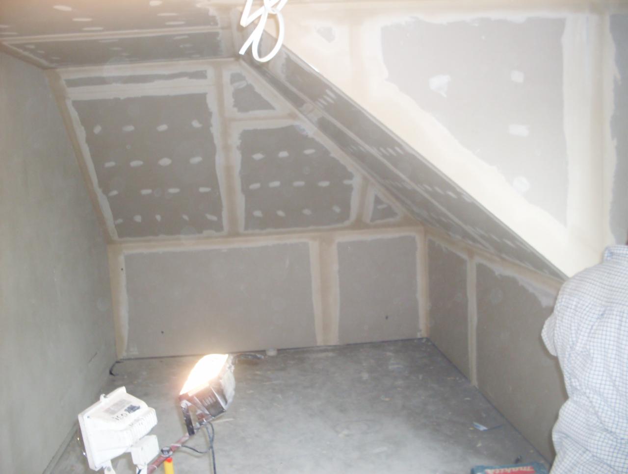 Poddasze w trakcie wykańczania płytami kartonowo-gipsowymi, widoczne łączenia płyt i lampa halogenowa oświetlająca wnętrze.