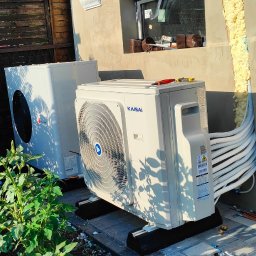 YOUVENT Michał Graczek - Dwa białe klimatyzatory Kaisai zamontowane na zewnątrz budynku, widoczne przewody i narzędzia, sugerujące trwający montaż. Tło: ściana budynku z oknem i fragment ogrodu.