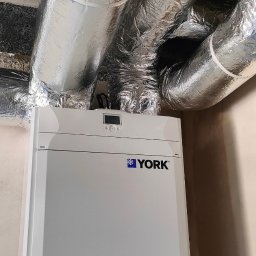 YOUVENT Michał Graczek - Biała jednostka klimatyzacyjna York z ekranem i rurami w izolacji aluminiowej pod sufitem. Widok z dołu, instalacja w pomieszczeniu.