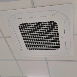 YOUVENT Michał Graczek - Kasetonowa klimatyzacja sufitowa LG w biurze, widok z dołu. Biała obudowa urządzenia wkomponowana w biały sufit podwieszany. Część sufitu jest uszkodzona.