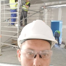 YOUVENT Michał Graczek - Instalacja wentylacji w budynku komercyjnym. Pracownicy na rusztowaniu montują srebrne rury wentylacyjne pod sufitem. Jeden z pracowników robi selfie.