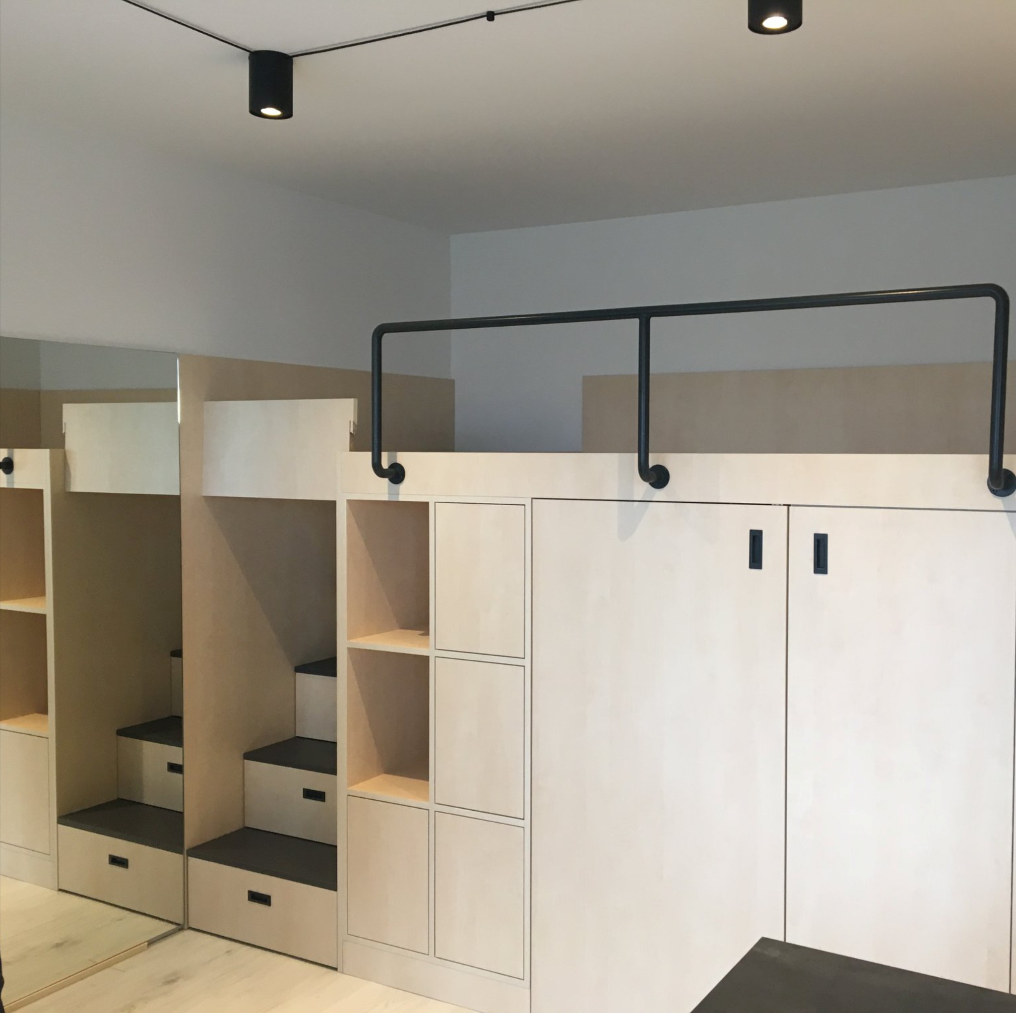 Funkcjonalna zabudowa meblowa w jasnym pokoju z łóżkiem na antresoli, schodami z szufladami i szafkami z minimalistycznymi uchwytami.