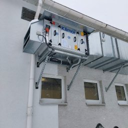 IMES Instalacje Sp. z o.o. - Zewnętrzna instalacja rekuperacji marki Klimor na ścianie budynku w zimowej scenerii, widoczna drabina sugerująca prace montażowe lub serwisowe.