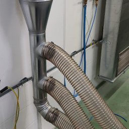 IMES Instalacje Sp. z o.o. - Metalowy przewód wentylacyjny z dwoma elastycznymi rurami podłączonymi do instalacji w pomieszczeniu technicznym.