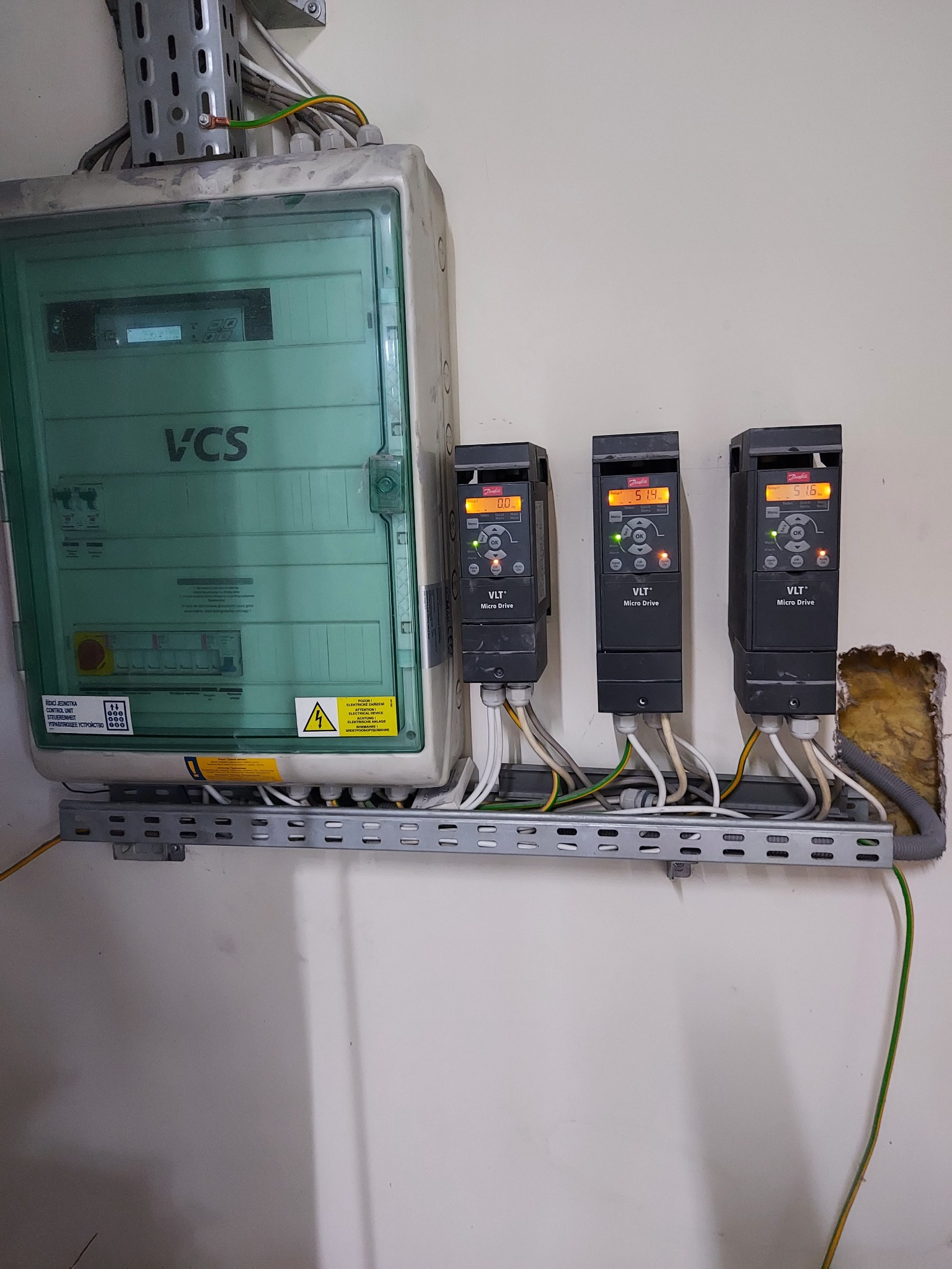 Panel sterowania z trzema falownikami VLT Micro Drive zamontowanymi na szynie. Widoczne okablowanie i oznaczenia ostrzegawcze na obudowie panelu.