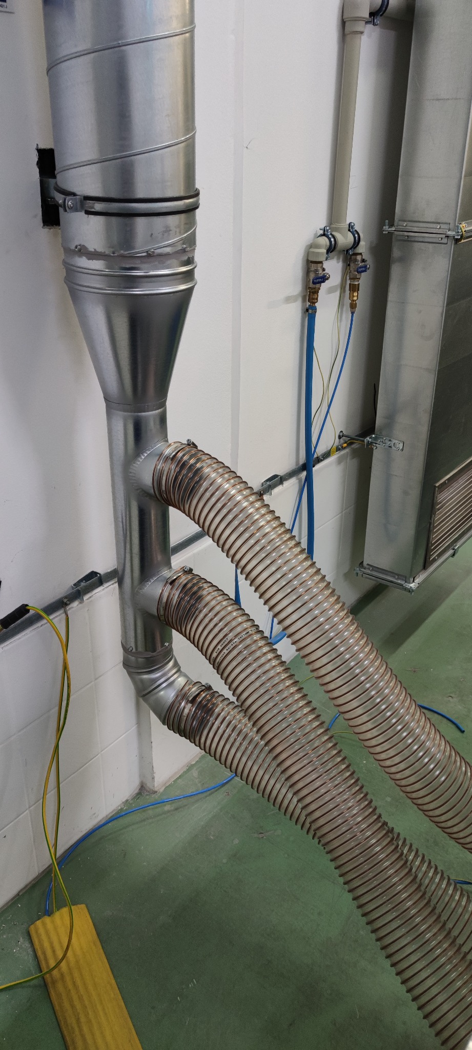 Metalowy przewód wentylacyjny z dwoma elastycznymi rurami podłączonymi do instalacji w pomieszczeniu technicznym.