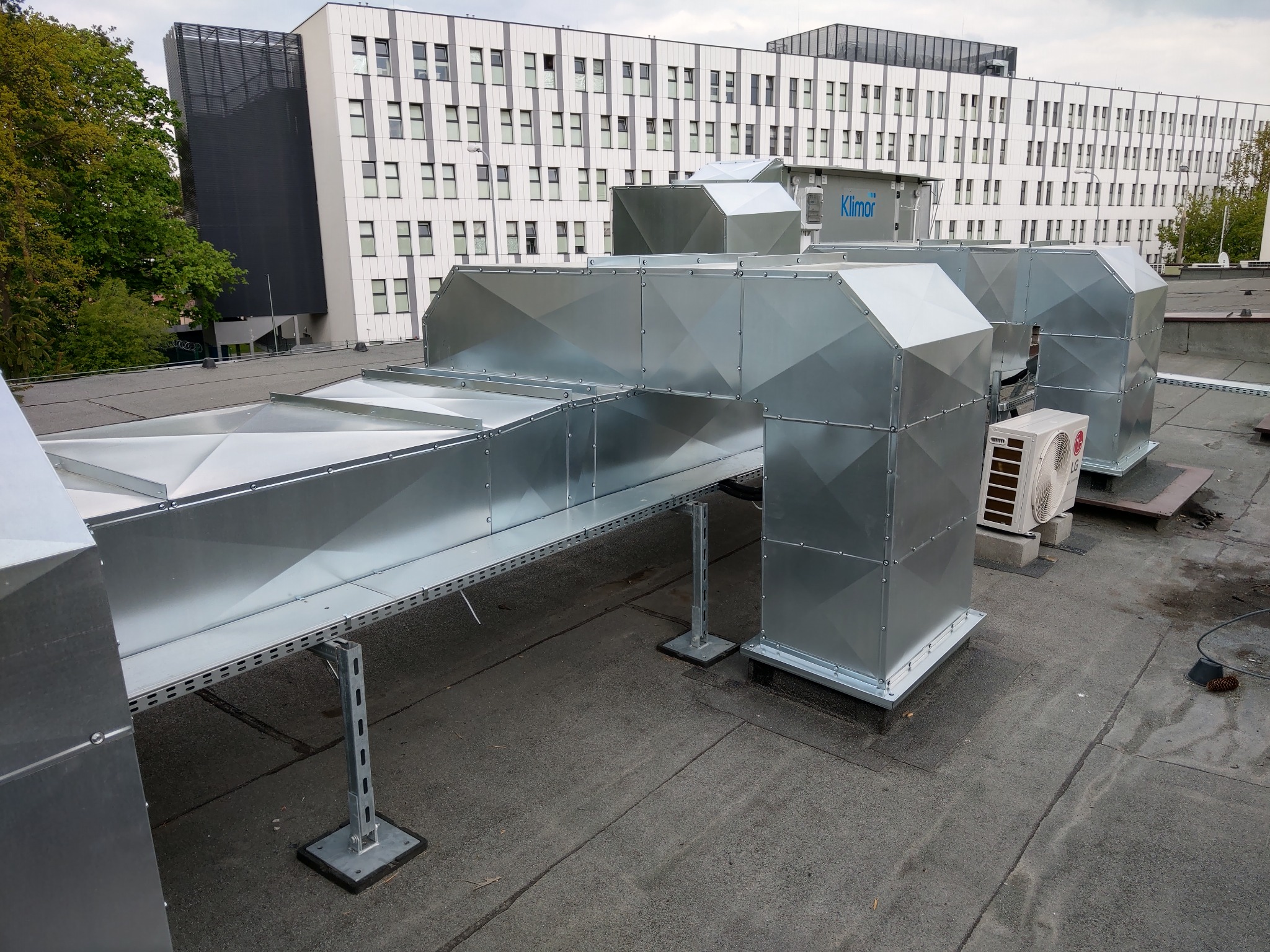Instalacja wentylacyjna z ocynkowanej blachy na dachu budynku biurowego, widoczne kanały wentylacyjne, klimatyzatory oraz logo firmy Klimor na jednym z elementów.