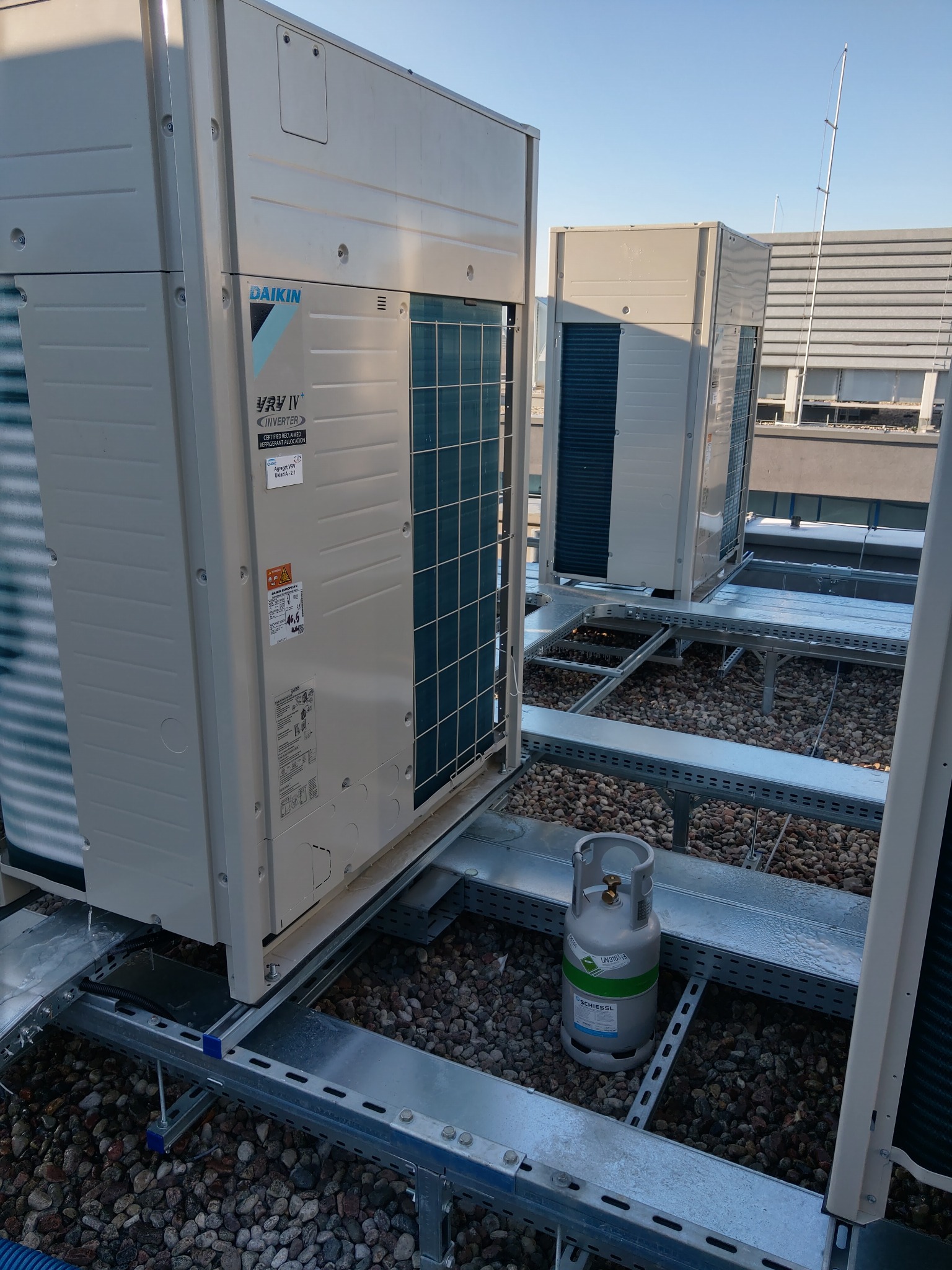 Dwa agregaty klimatyzacyjne Daikin VRV IV na dachu budynku komercyjnego, zamontowane na metalowej konstrukcji, obok butla z czynnikiem chłodniczym Schiessl, widoczne elementy instalacji odgromowej.