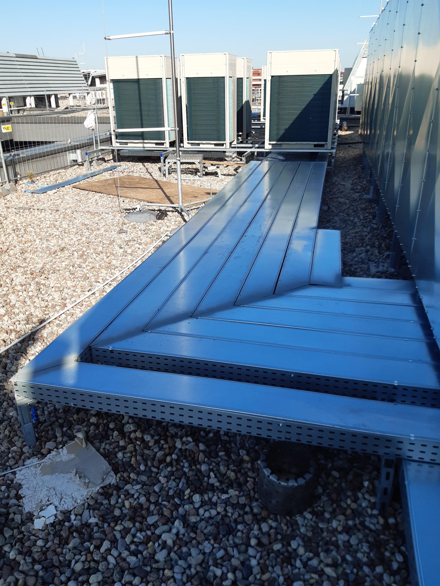 Instalacja przemysłowej klimatyzacji na dachu budynku, widoczne jednostki zewnętrzne i metalowa platforma serwisowa na żwirowym podłożu.