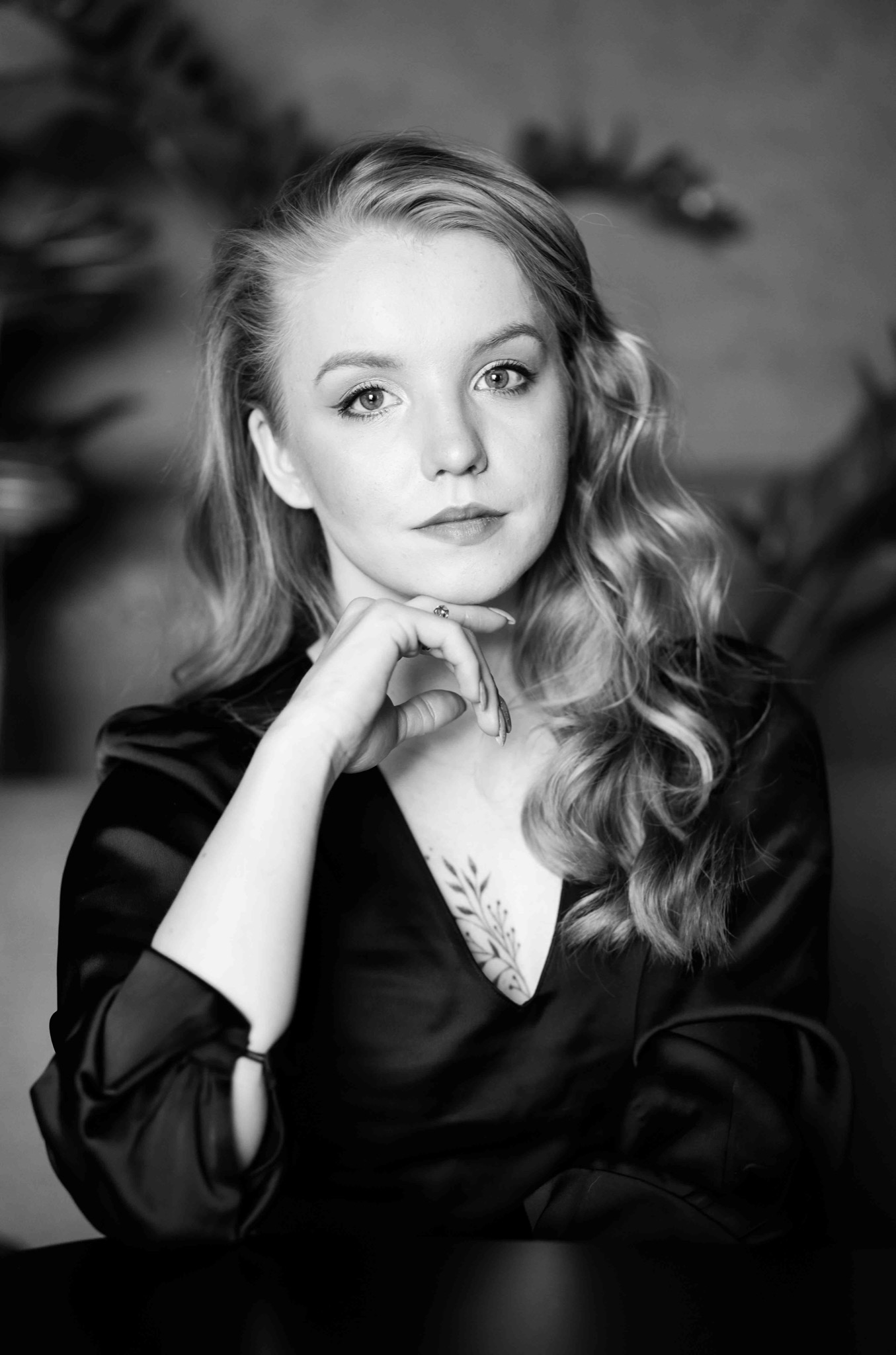 Portret kobiety z tatuażem roślinnym na dekolcie, opierającej brodę na dłoni, wykonany w Łodzi w czerni i bieli.