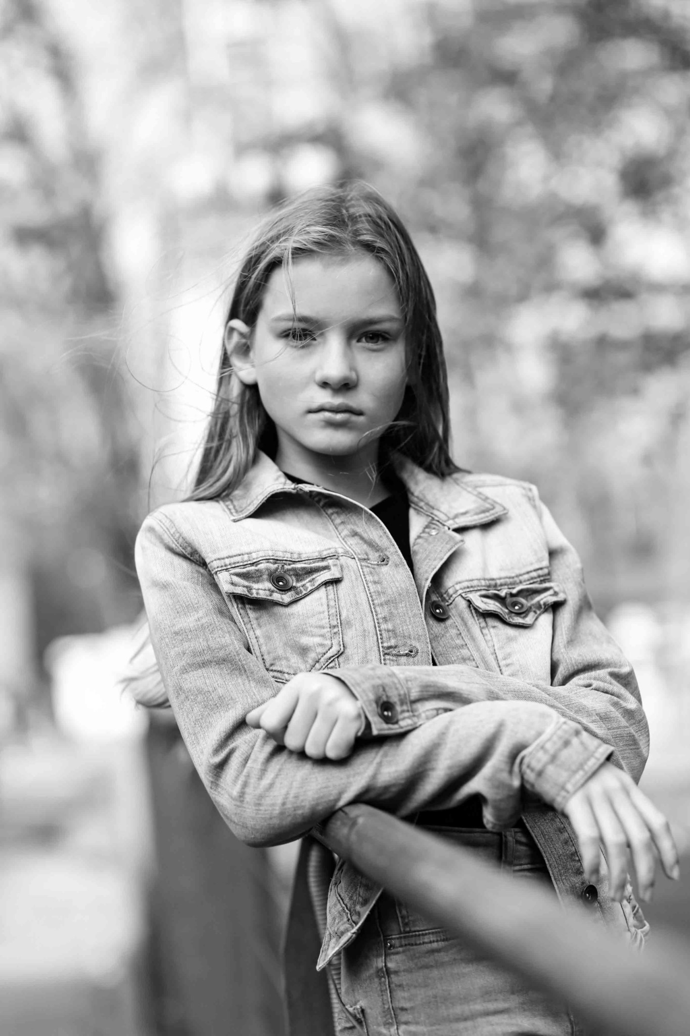 Portret młodej dziewczyny w dżinsowej kurtce, opierającej się o barierkę, w czarno-białej tonacji.