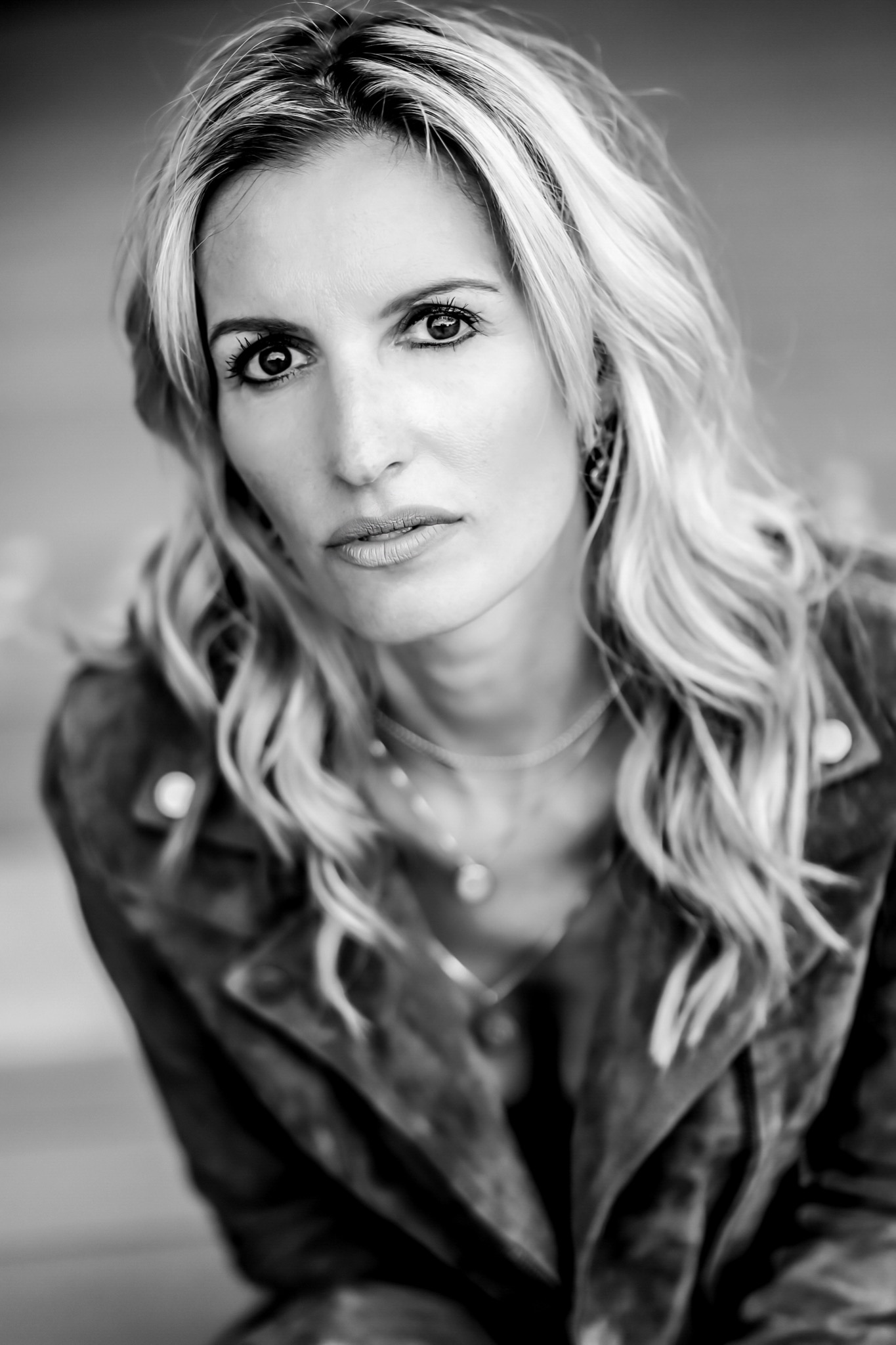 Portret kobiety o jasnych włosach, z intensywnym spojrzeniem, ubrana w skórzaną kurtkę, czarno-białe zdjęcie z delikatnym ziarnem.