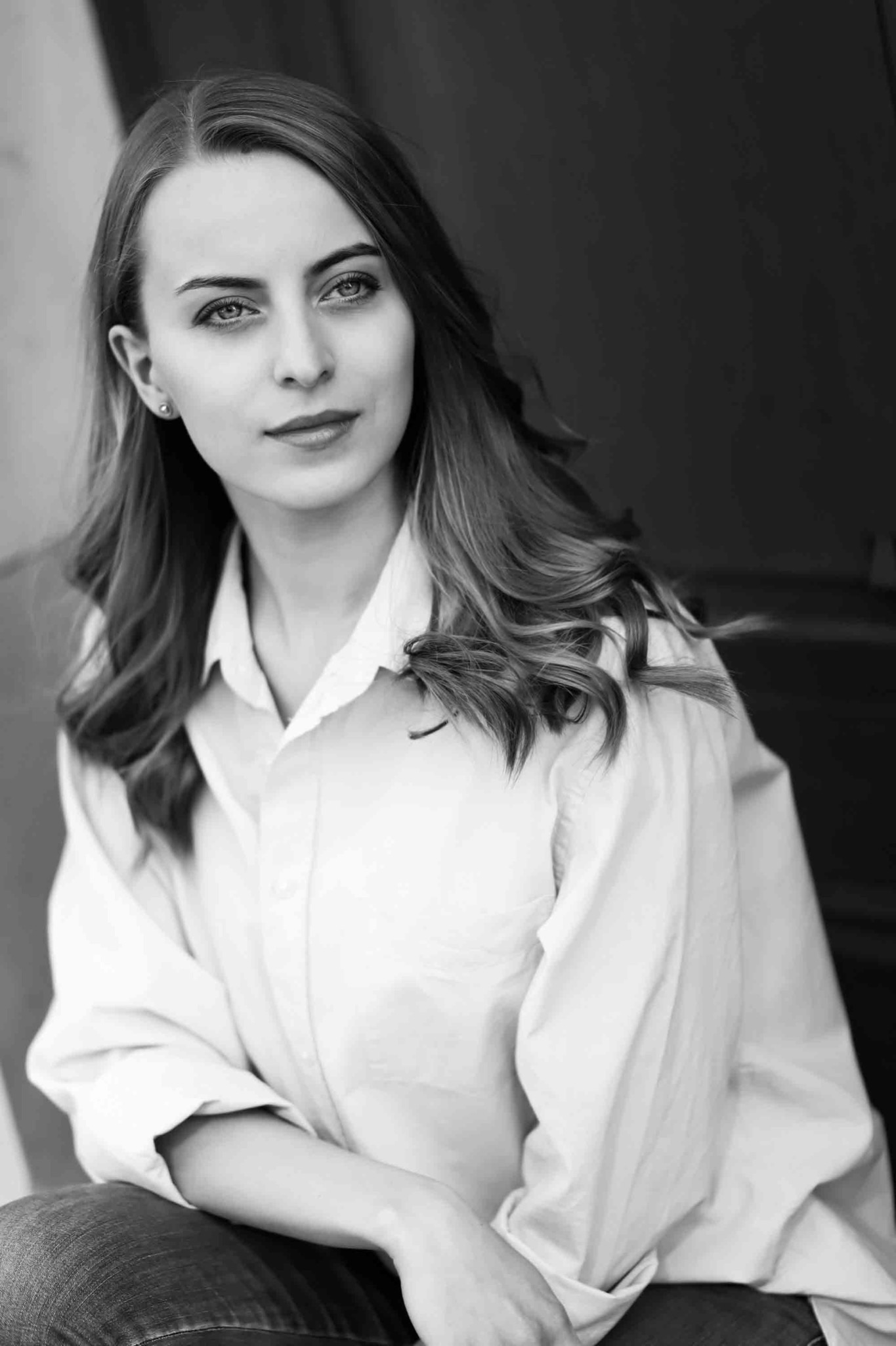 Portret młodej kobiety w białej koszuli, czarno-białe zdjęcie z delikatnym uśmiechem i długimi, falowanymi włosami.
