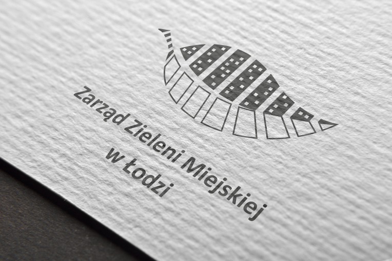 Logo Zarządu Zieleni Miejskiej w Łodzi przedstawione jako liść z budynkami wewnątrz, na teksturowanym papierze.