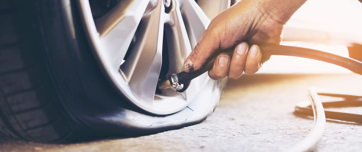 Pompowanie opony samochodowej z użyciem węża, widoczna dłoń i metalowa felga.
