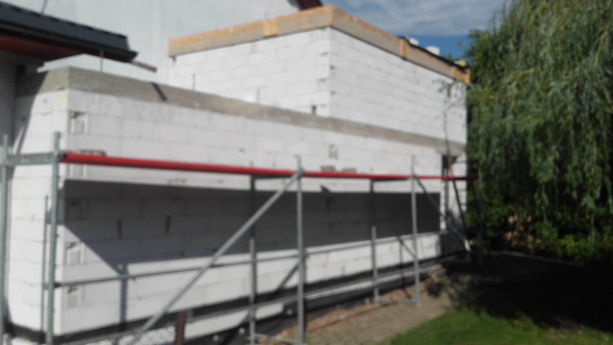 Budowa domu z białych bloczków, widoczne rusztowanie na tle zieleni