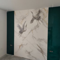 KP Remonty Kamil Pierzakowski - Ściana w Dobiegniewie z dekoracyjnym malowaniem imitującym marmur z motywem żurawi w locie, obok pionowe pasy w kolorze butelkowej zieleni, widoczne gniazdka elektryczne.