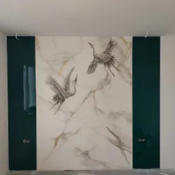 Ściana z marmurowym wzorem i motywem żurawi, obok pionowe pasy ciemnozielonego lakierowanego panelu, widoczne gniazdka elektryczne, surowy stan wykończenia.