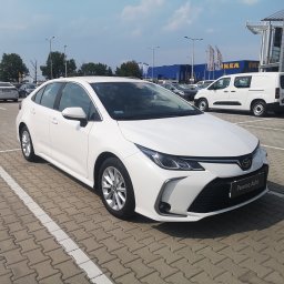 GO CAR TAXI MAŁGORZATA MAJCHROWICZ - Biała Toyota Corolla zaparkowana na parkingu przed sklepem IKEA i Castorama, widoczny napis 'Pewne Auto' na tabliczce dealera.