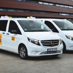 GO CAR TAXI MAŁGORZATA MAJCHROWICZ - Dwa białe busy Mercedes-Benz Vito z oznaczeniami taxi Wicar, zaparkowane przed nowoczesnym budynkiem z ciemnego drewna i szkła we Wrocławiu, z widocznymi tablicami rejestracyjnymi DW 5FL94 i DW 1NM13.