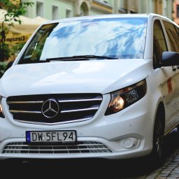 GO CAR TAXI MAŁGORZATA MAJCHROWICZ - Biały Mercedes Vito z polską tablicą rejestracyjną DW 5FL94 zaparkowany na brukowanej ulicy, widoczny numer boczny 901, w tle parasole kawiarniane i budynki.