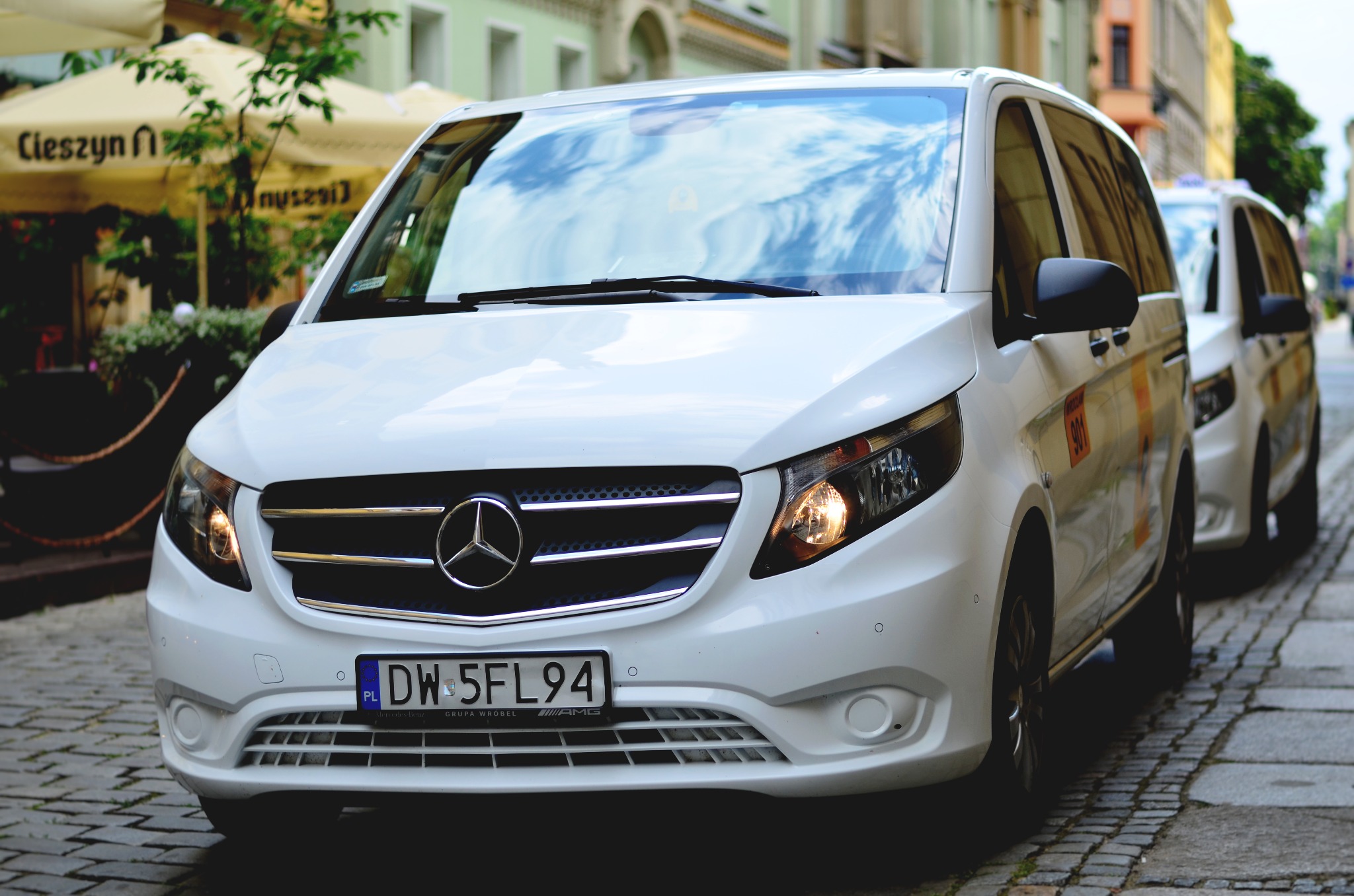Biały Mercedes Vito z polską tablicą rejestracyjną DW 5FL94 zaparkowany na brukowanej ulicy, widoczny numer boczny 901, w tle parasole kawiarniane i budynki.