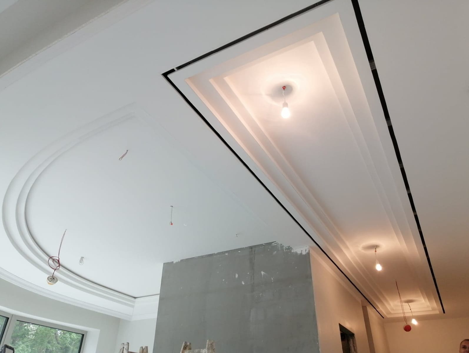 Biały sufit z dekoracyjnymi elementami gipsowymi i oświetleniem, widoczne niedokończone ściany w tle.