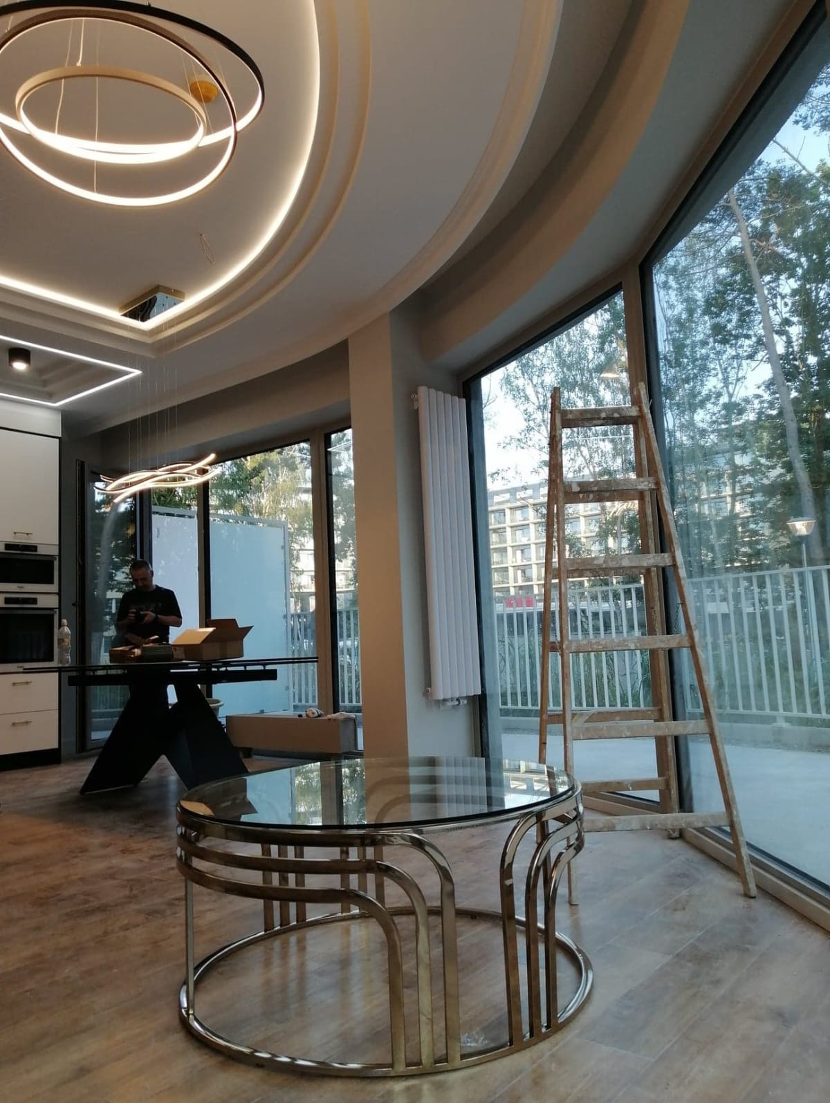 Jasne wnętrze z nowoczesnym oświetleniem sufitowym, drewnianą drabiną opartą o duże okno i pracującym mężczyzną w tle, częściowo wyposażone.