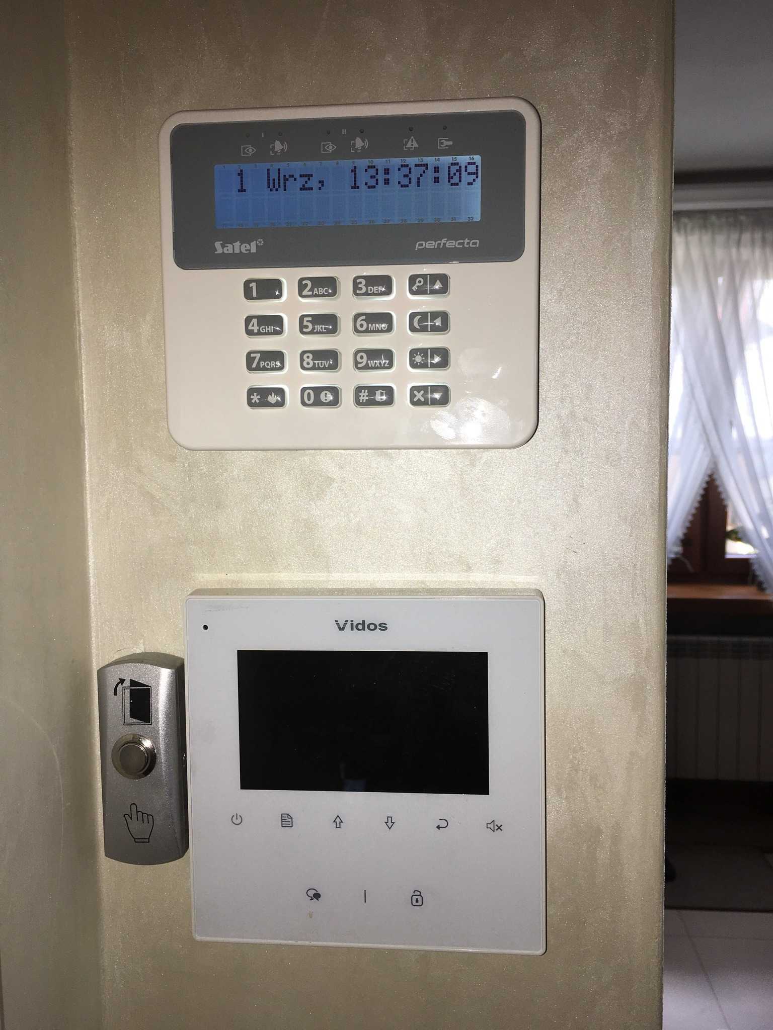Zamontowany na ścianie manipulator systemu alarmowego Satel Perfecta, pod nim monitor systemu wideodomofonowego Vidos wraz z przyciskiem otwierania drzwi.