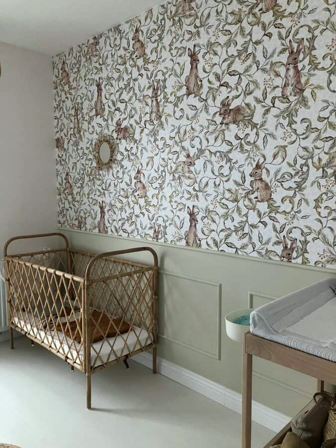 Pokój dziecięcy z tapetą w króliki i liście, rattanowe łóżeczko i przewijak w pastelowych odcieniach zieleni i bieli.