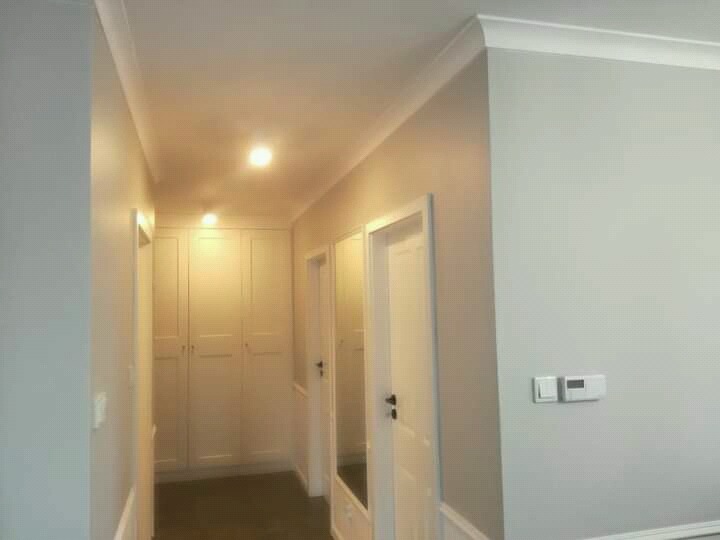 Korytarz w odcieniach szarości i bieli z zabudowaną szafą na końcu, widoczne listwy przypodłogowe i oświetlenie sufitowe.