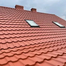 Czerwony dach z blachodachówki z dwoma oknami dachowymi i dwoma kominami z cegły, widok z dołu pod kątem.