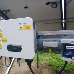 VOLT-MAR usługi elektryczne Marek Kierepka - Falownik Sofar i rozdzielnica PV-AC Noark zamontowane na konstrukcji fotowoltaicznej, widoczne kable i przewody elektryczne, ostrzeżenia o wysokim napięciu.