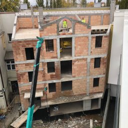 DM BUDOWNICTWO S.C. - Wysoki kąt na budowę z cegły z dźwigiem. Murarze w żółtych kamizelkach pracują na górze. Widoczne okna i elementy konstrukcyjne. Pochmurne niebo w tle.