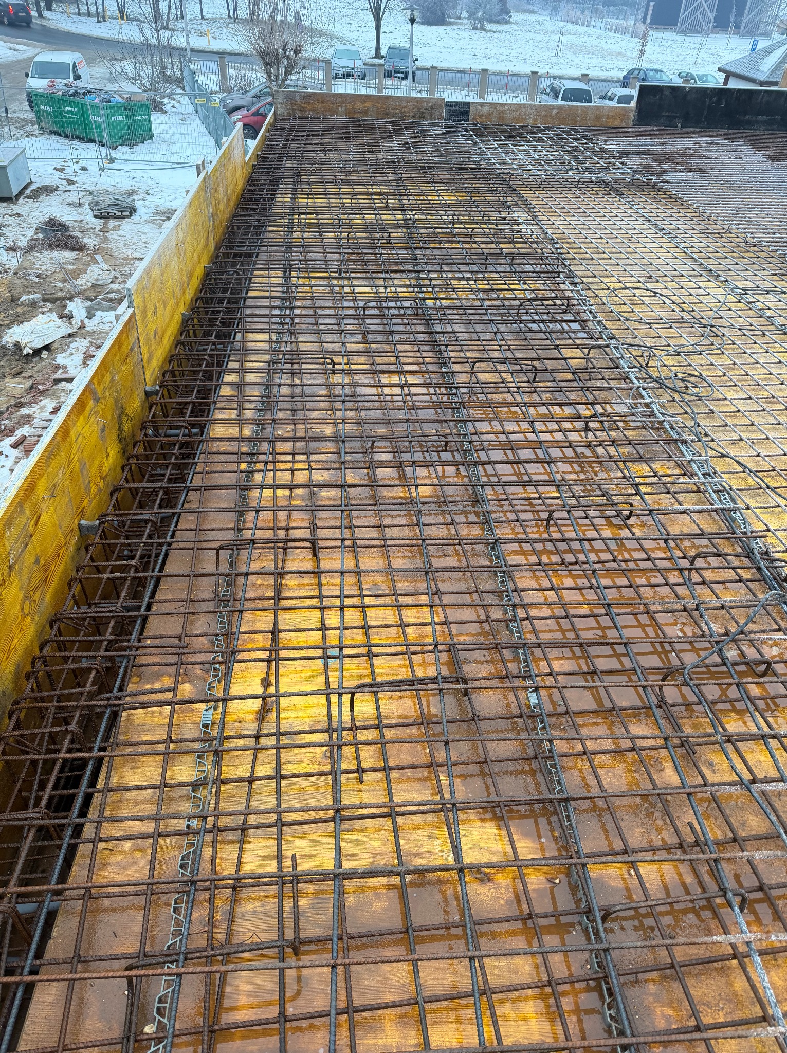 Siatka zbrojeniowa ułożona na szalunku z żółtych płyt, przygotowana do zalania betonem. Widoczne elementy dystansowe. W tle zimowy krajobraz.