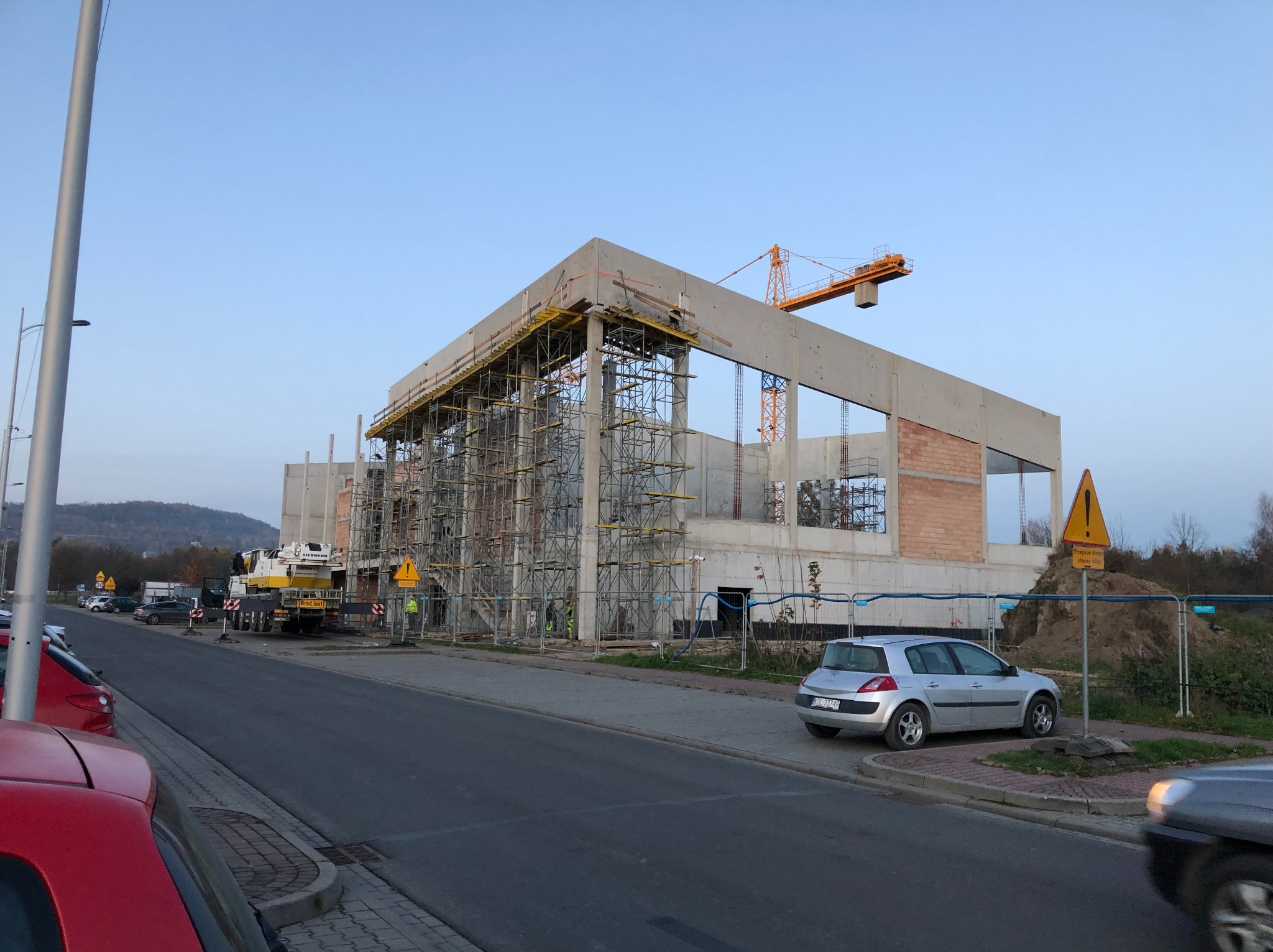 Budowa budynku żelbetowego w Krakowie, widok z ulicy. Konstrukcja w trakcie wznoszenia, widoczne rusztowania i dźwig. Częściowo wymurowane ściany.