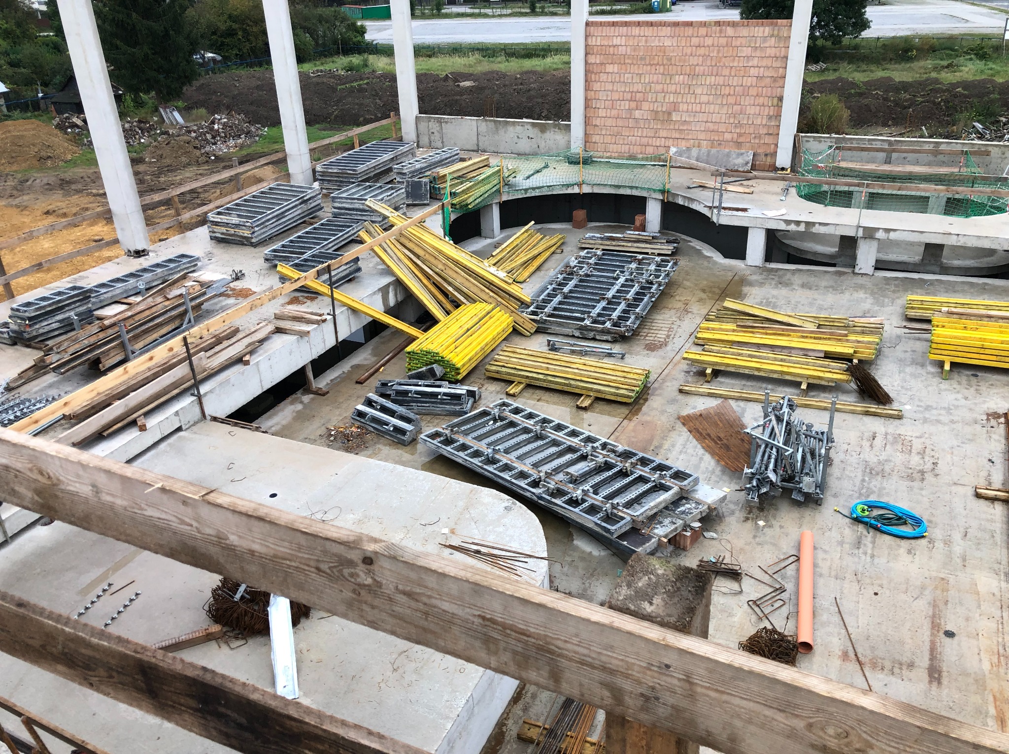 Budowa w toku: widok z góry na betonowy strop z przygotowanymi szalunkami, drewnianymi belkami i zbrojeniami. W tle widoczne elementy konstrukcyjne i teren budowy.