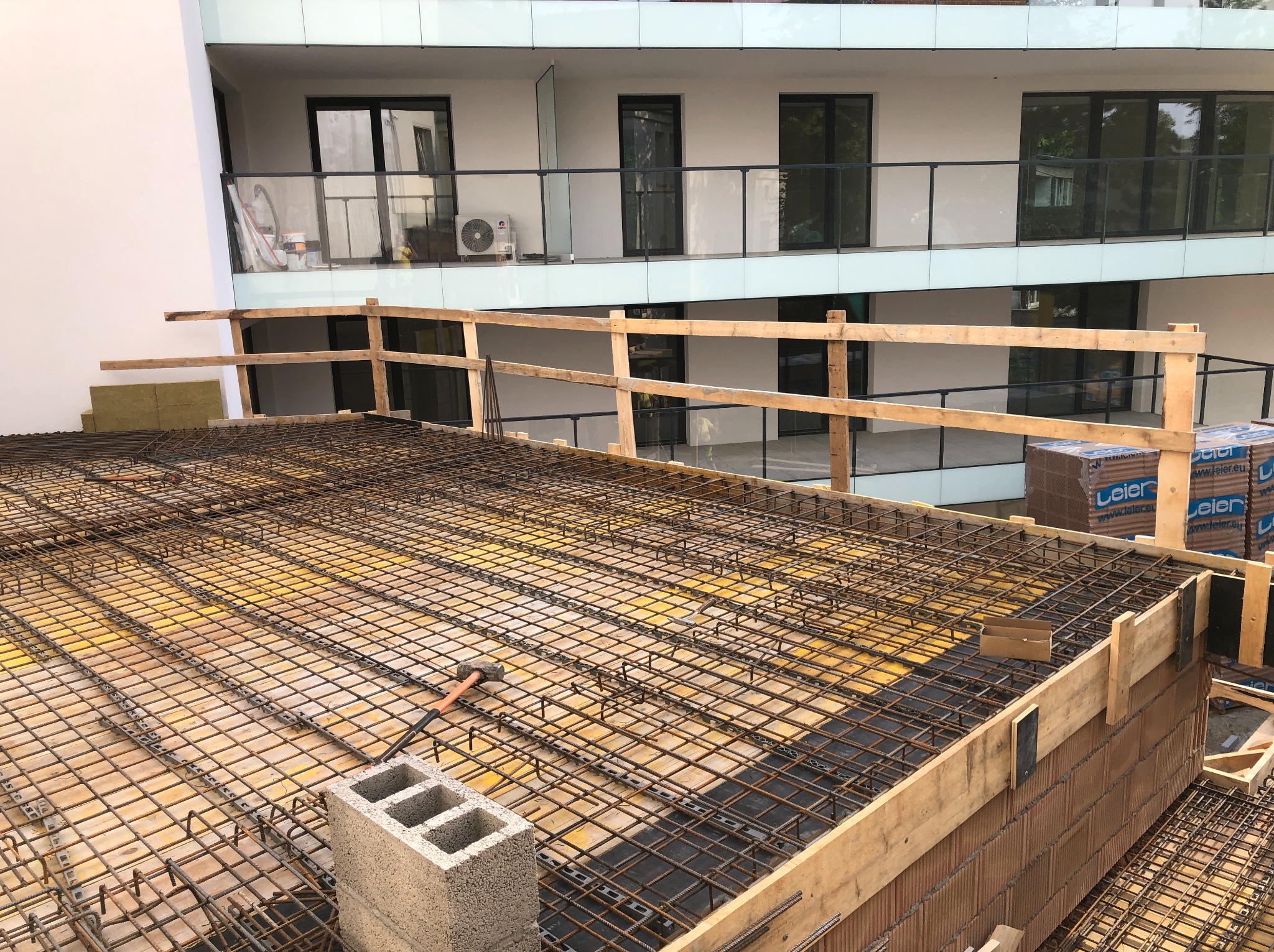 Zbrojenie stropu na budowie wielorodzinnego budynku z widocznymi bloczkami Leier, deskowaniem i fragmentem rusztowania. W tle elewacja z balkonami.