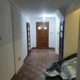 Korytarz po remoncie z dekoracyjną ścianą z białej cegły, brązowymi płytkami podłogowymi i widocznym zabezpieczeniem podłogi folią malarską.