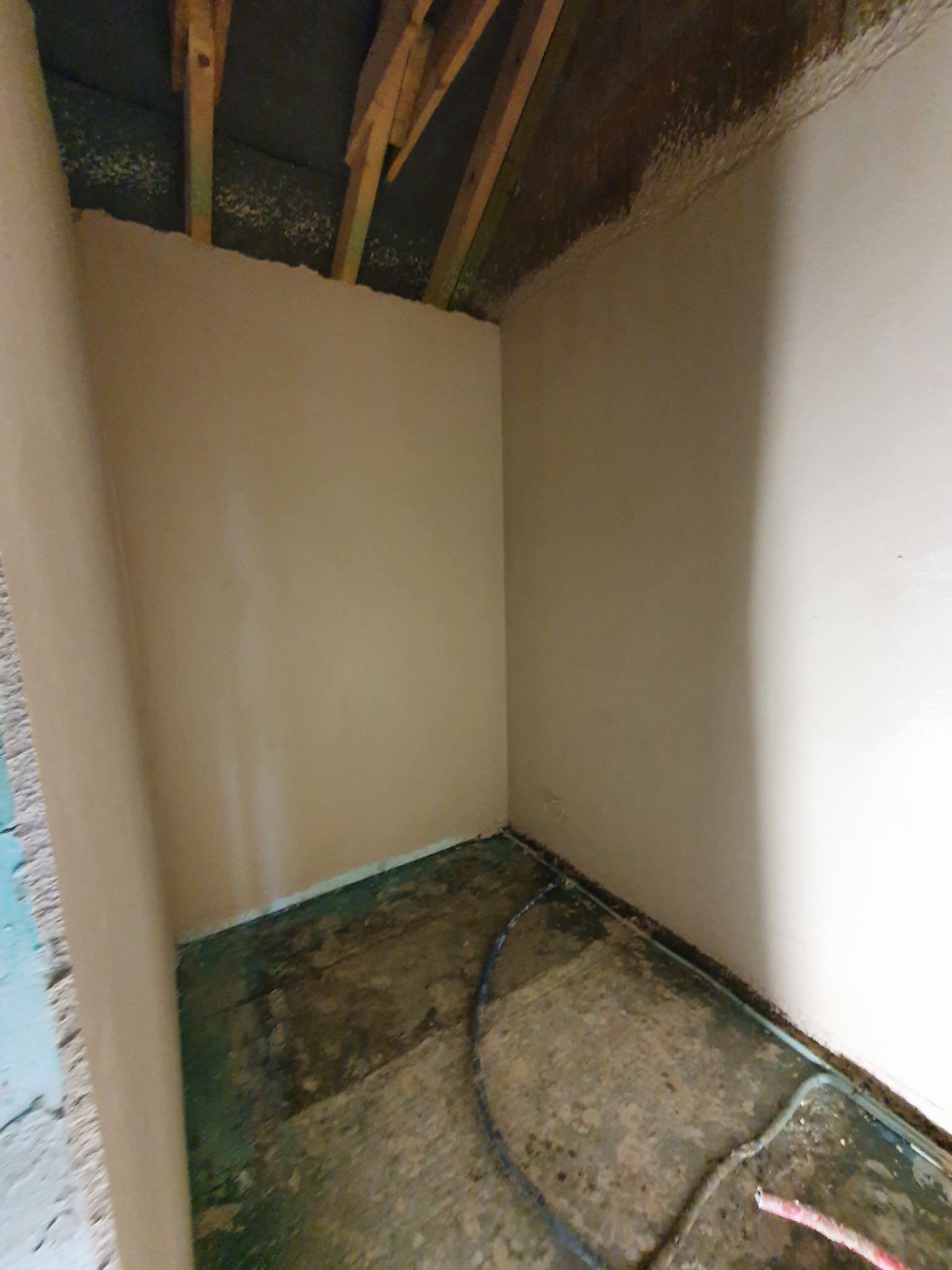 Wnętrze pomieszczenia w trakcie prac wykończeniowych, świeżo otynkowane ściany w odcieniach beżu i bieli, widoczne drewniane elementy konstrukcyjne pod sufitem, podłoga zabezpieczona folią...