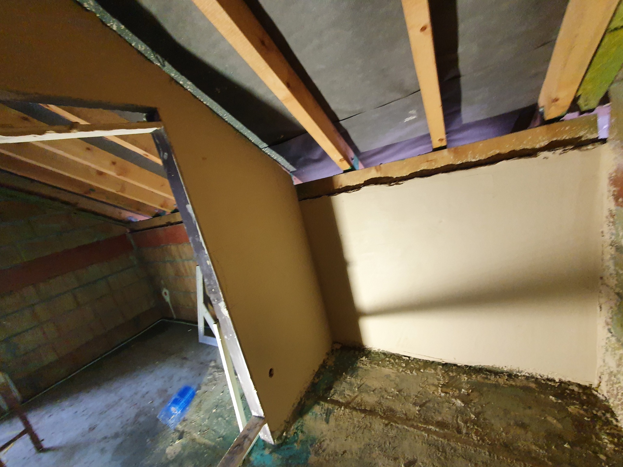 Tynkowanie poddasza w trakcie prac w Turku: widoczne surowe ściany z cegły, drewniane belki stropowe i fragment świeżo nałożonego tynku na ścianie szczytowej.