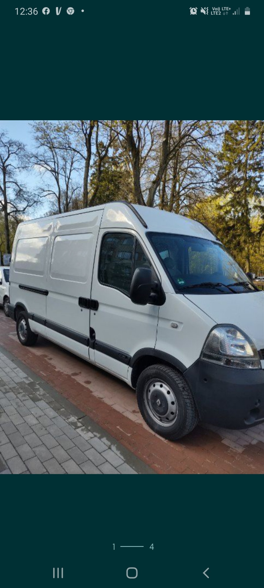 Biały samochód dostawczy Renault Master zaparkowany na chodniku z kostki, widok z boku, drzewa w tle.