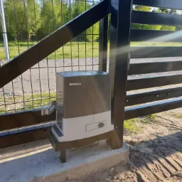 Zamontowany napęd Beninca do bramy wjazdowej, widoczny mechanizm i zębatka, tło z zielenią.