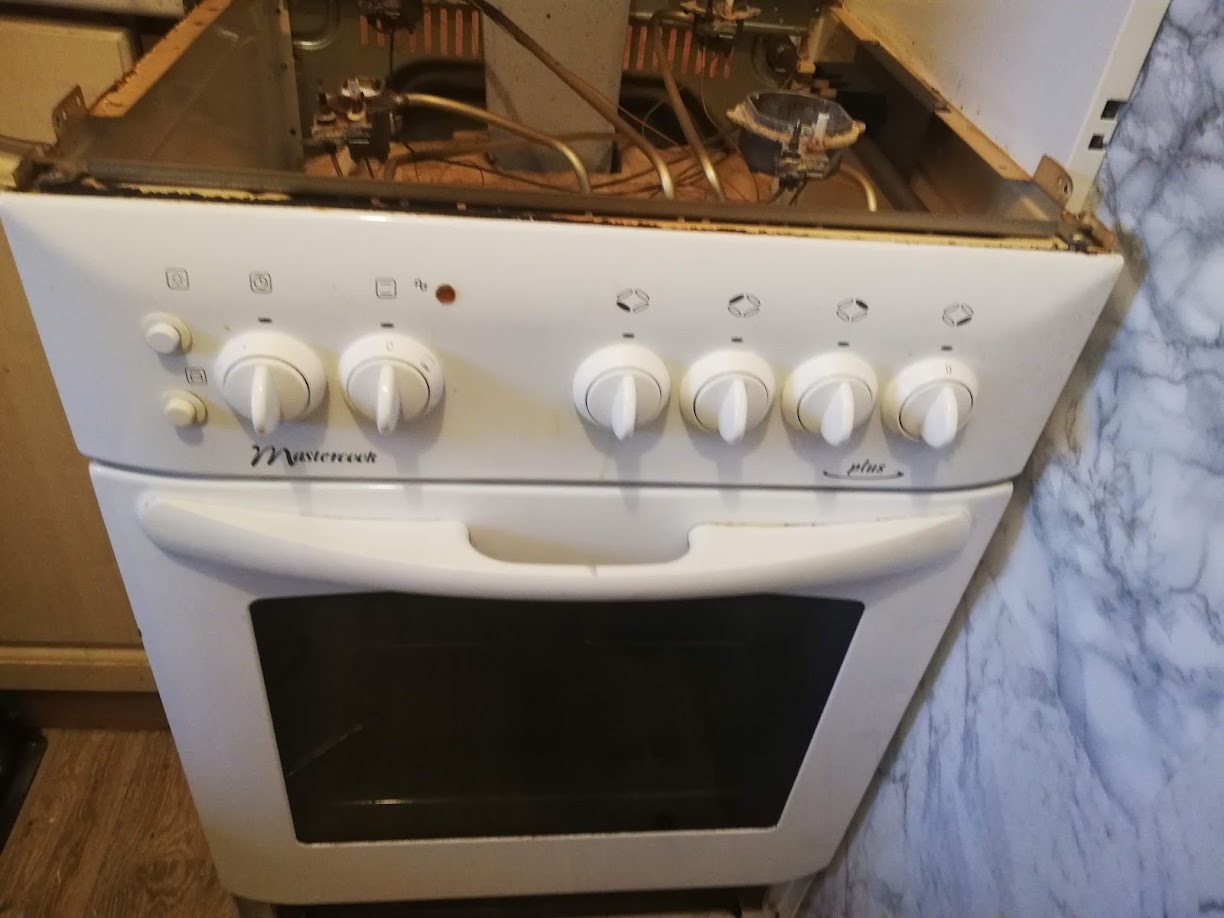 Biała kuchenka Mastercook Plus z otwartą górną częścią, ukazującą elementy wewnętrzne, potencjalnie w trakcie serwisu lub naprawy.