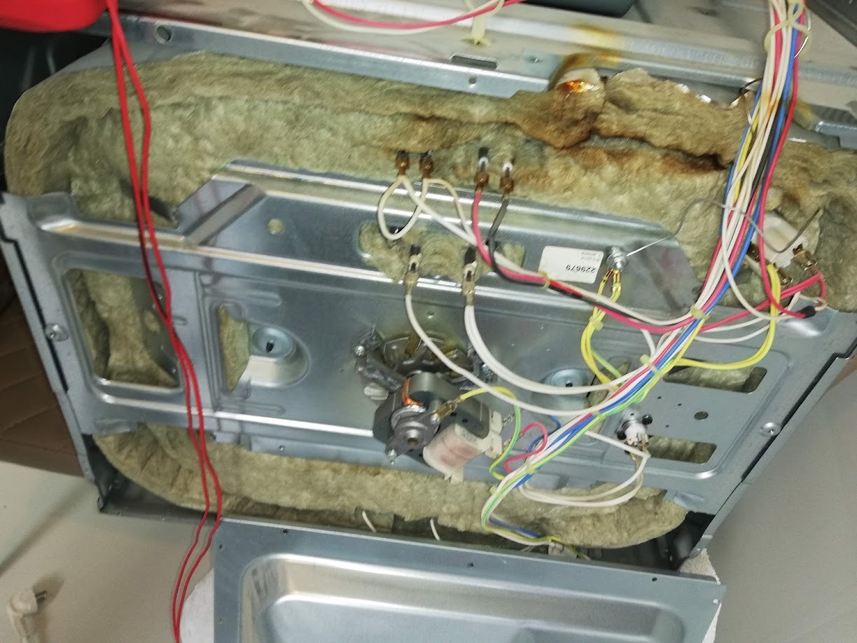 Wnętrze piekarnika z widoczną izolacją termiczną, przewodami elektrycznymi i elementami grzejnymi, w trakcie naprawy lub demontażu.