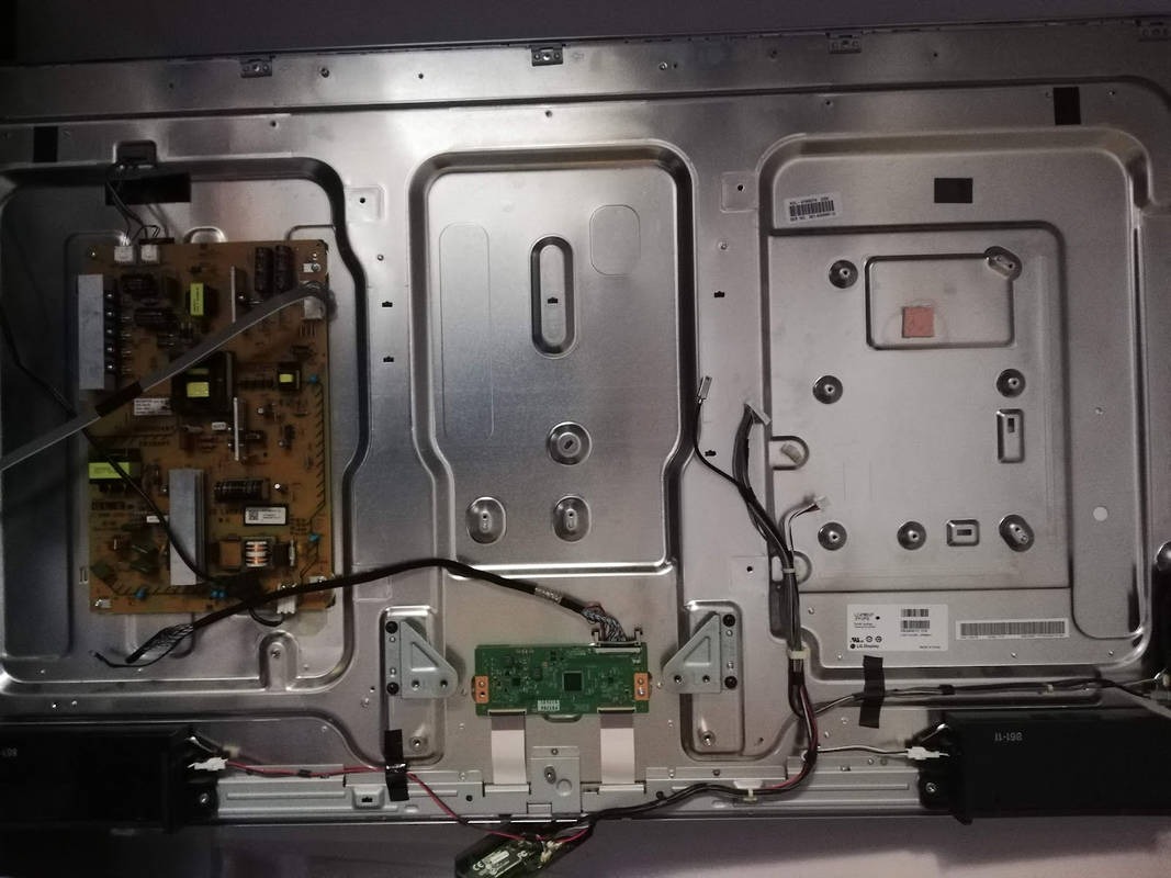 Wnętrze obudowy telewizora z widocznymi płytkami drukowanymi, kablami i metalowymi elementami konstrukcyjnymi. Widoczne ślady po naklejkach i etykietach.