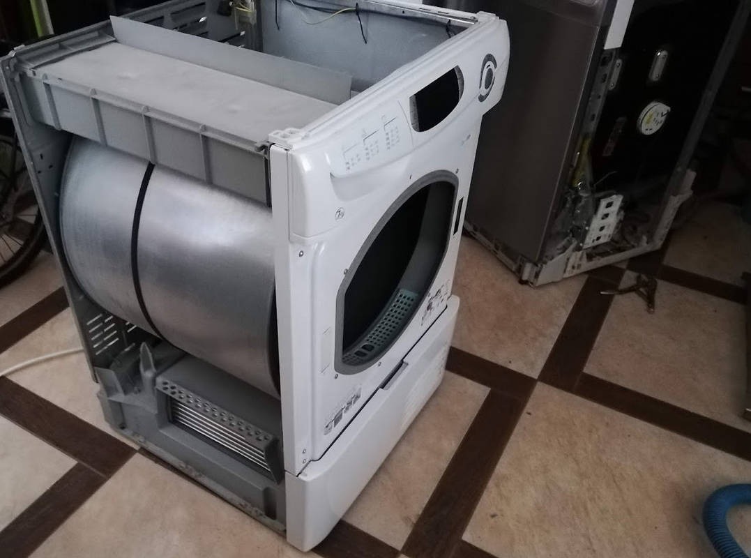 Rozłożona pralka automatyczna z widocznym bębnem i elementami obudowy, prawdopodobnie w trakcie naprawy lub demontażu, z drugim urządzeniem w tle.