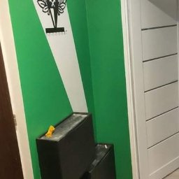 Siwy The Home - Pomieszczenie po malowaniu ścian na zielono z białym pasem i herbem Górnika Zabrze, widoczne dwa czarne pojemniki i fragment białych drzwi.