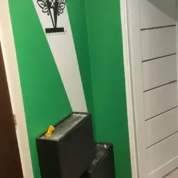 Pomieszczenie po malowaniu ścian na zielono z białym pasem i herbem Górnika Zabrze, widoczne dwa czarne pojemniki i fragment białych drzwi.